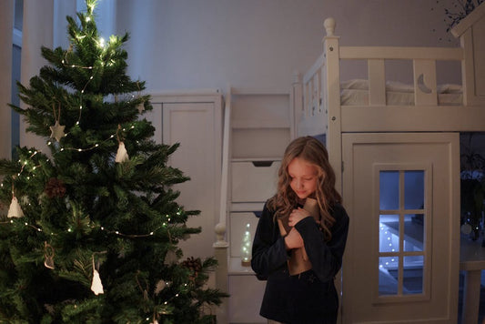 Young girl hugging a gift next to a decorated Christmas tree in a cozy room.